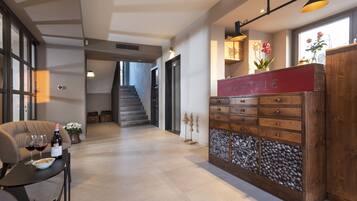 Ein Empfangsbereich mit einer Holztruhe mit dem Aufdruck "RECEPTION", einer Treppe im Hintergrund und einem Tisch mit Weingläsern und einer Schüssel Müsli.