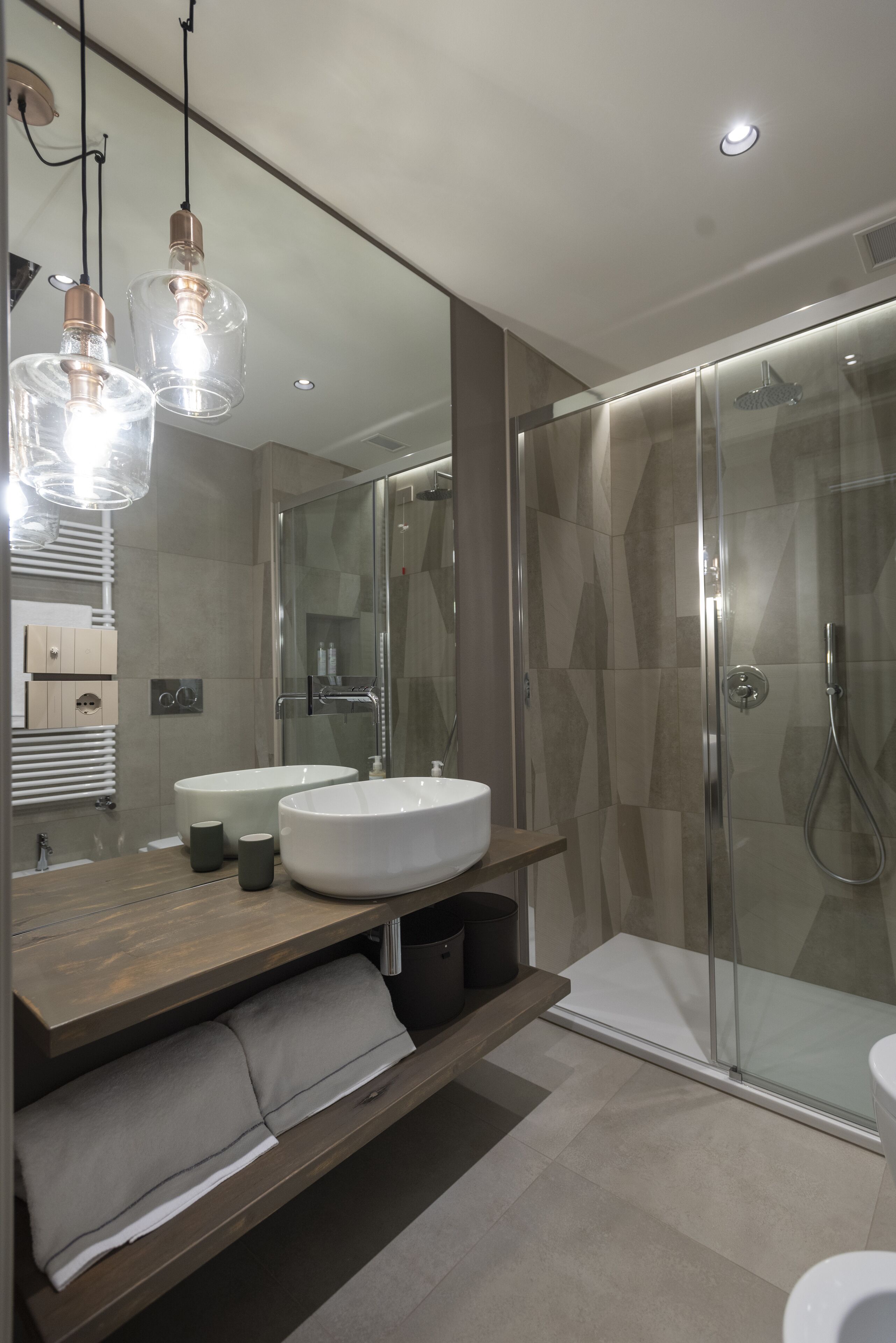 Un baño moderno con dos lavamanos amplios, un box de ducha de vidrio y un mueble de tocador de madera con espacio de almacenamiento.