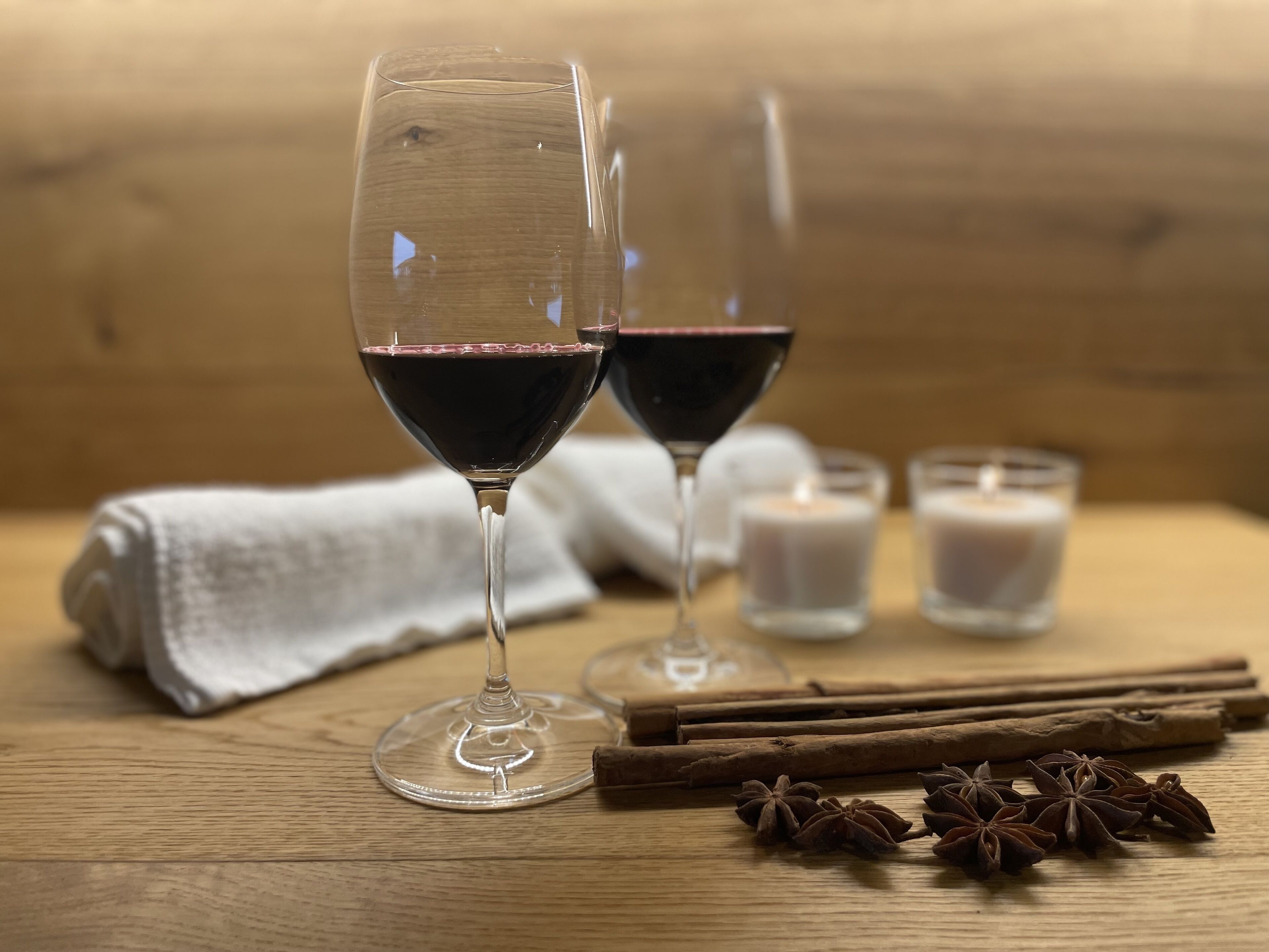 Dos copas de vino sobre una mesa de madera con mantel blanco, palitos de canela y anís estrellado.