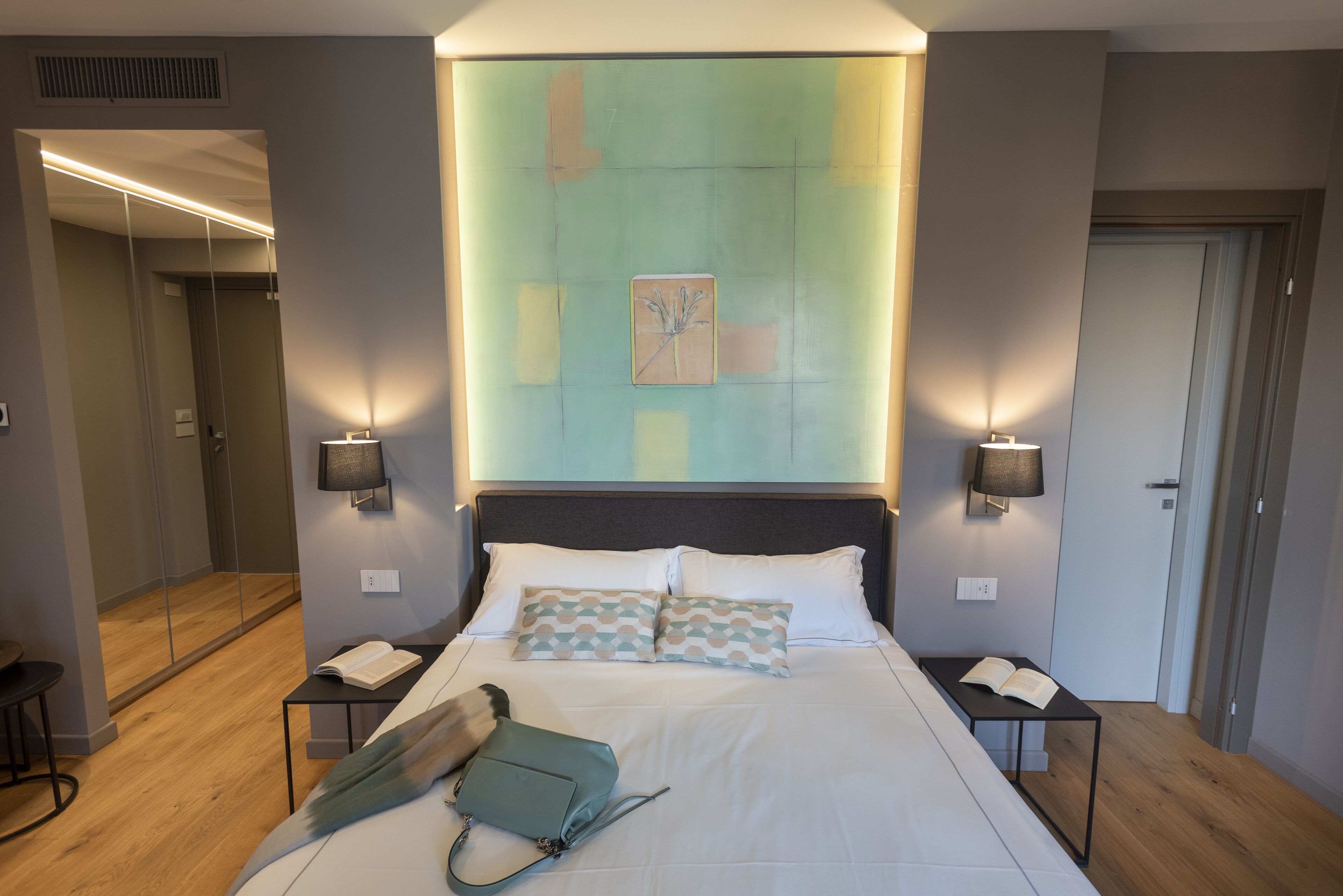 Habitación de hotel con una cama grande, mesitas de noche, un bolso verde y una obra de arte colgada en la pared.