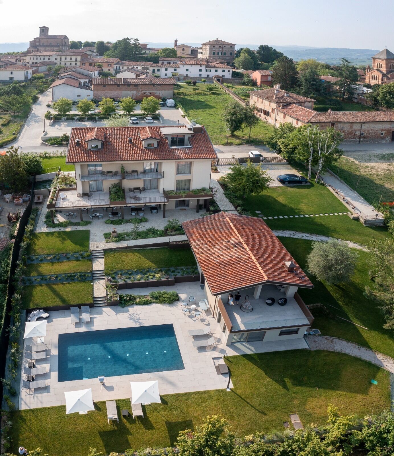 Ein zweistöckiges Haus mit Swimmingpool, umgeben von einem gepflegten Garten und Blick auf eine historische Stadt im Hintergrund.