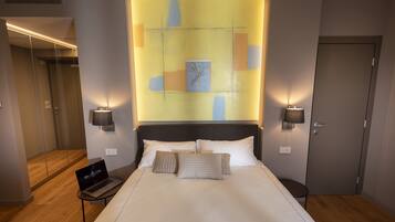 A modern hotel room with a large bed, a laptop on a side table, and a glass-enclosed shower area.