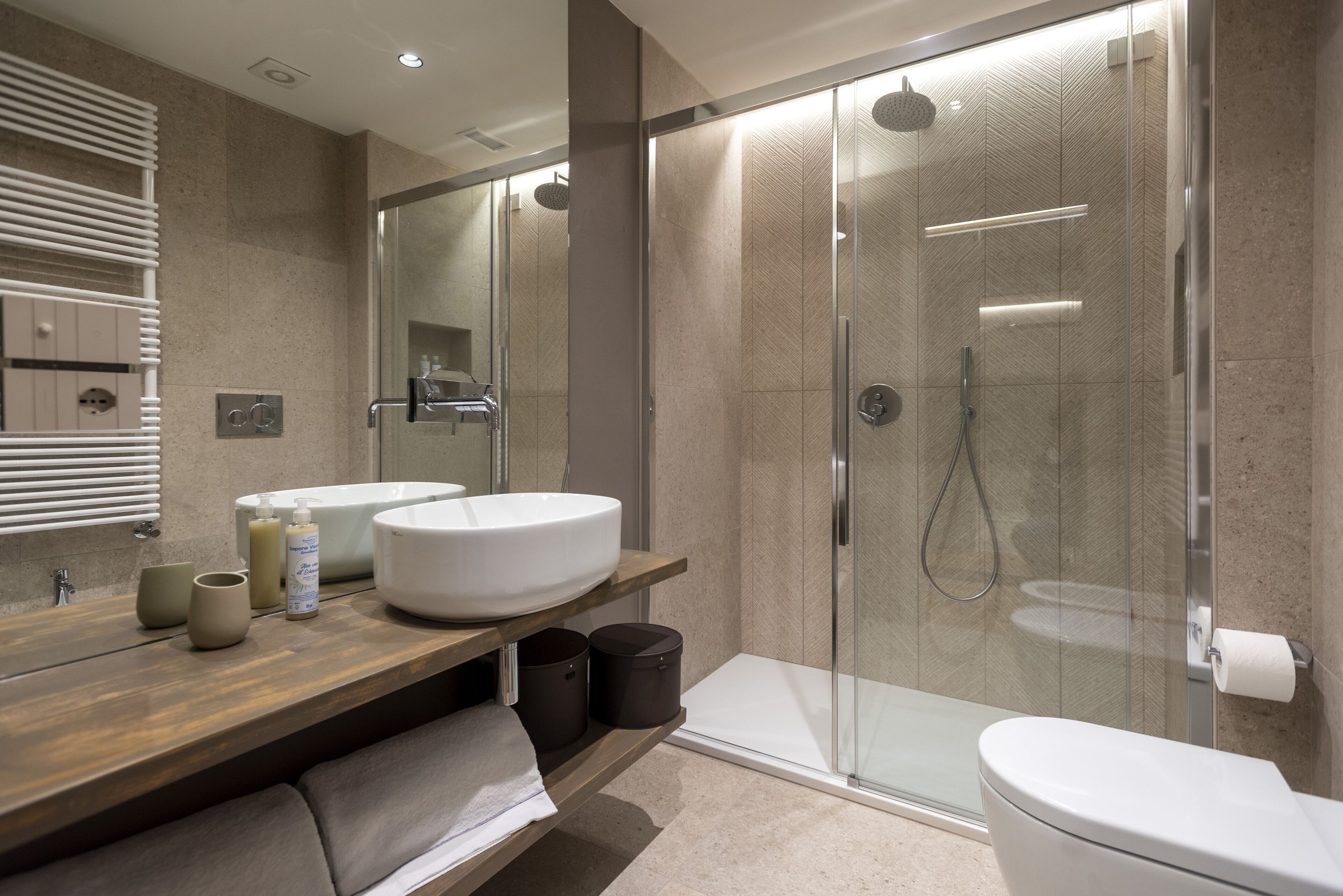 A modern bathroom with a large mirror, two sinks, a shower enclosure, and a toilet.