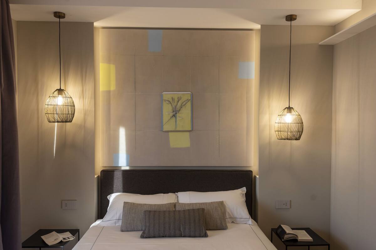 Una habitación de hotel con una cama, dos mesitas de noche y dos lámparas colgantes.