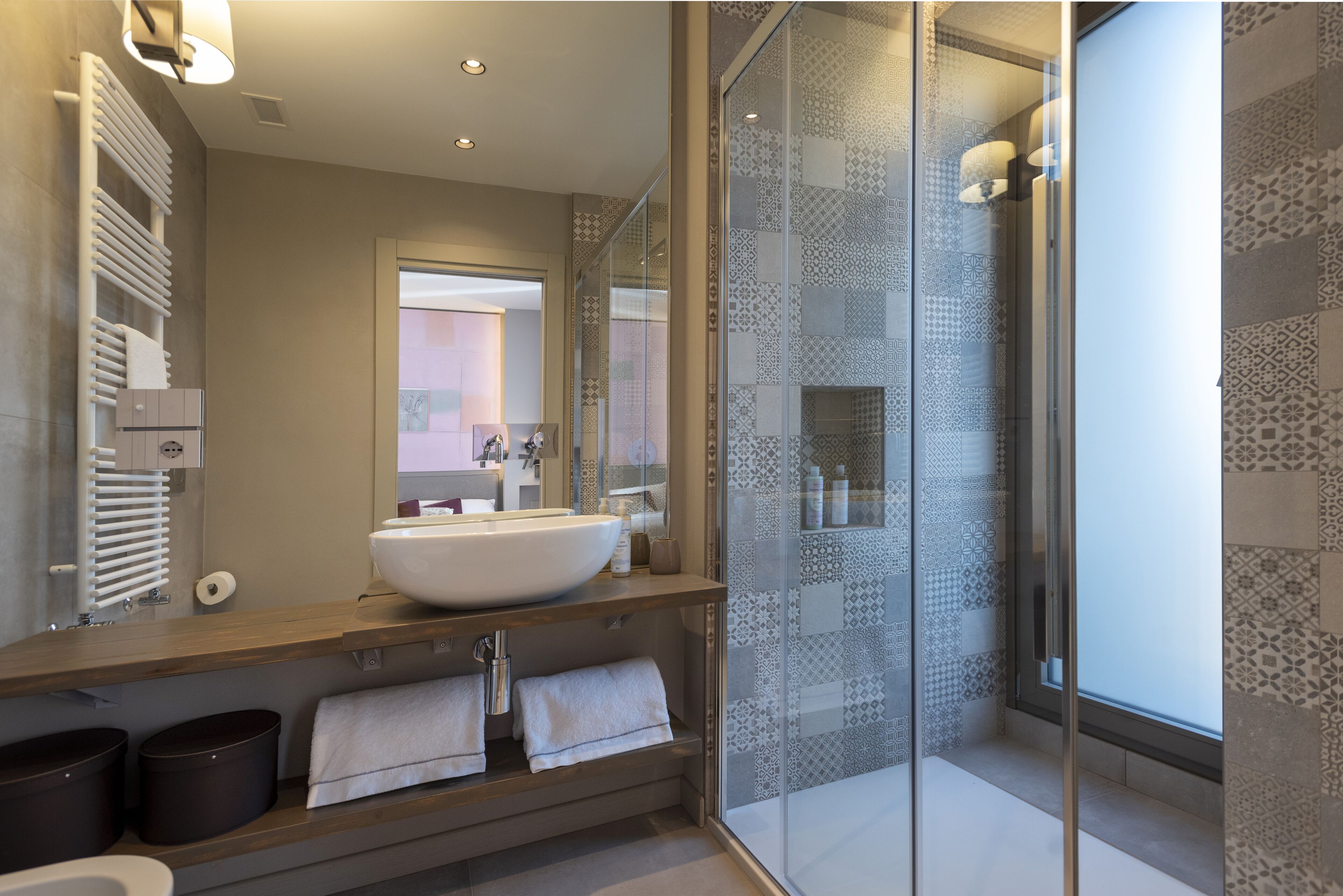 A modern bathroom with a large mirror, a vessel sink, a glass-enclosed shower, and patterned tiles.
