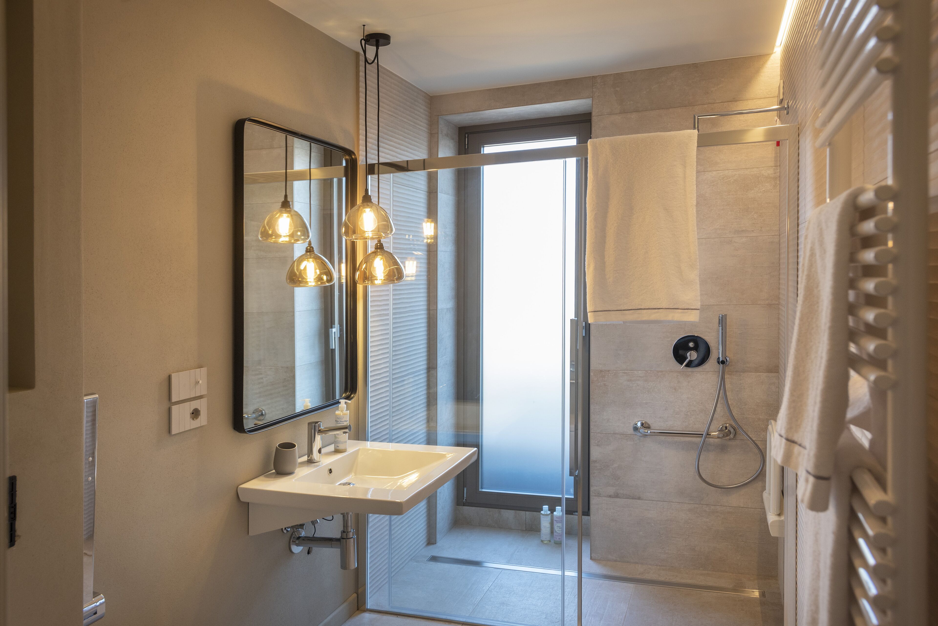 Une salle de bain moderne avec une douche à parois de verre, un lavabo blanc et des luminaires suspendus.