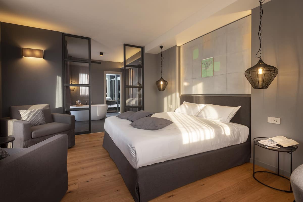 Un dormitorio moderno con una cama grande, una zona de estar con sofá, una mesita y un espejo.