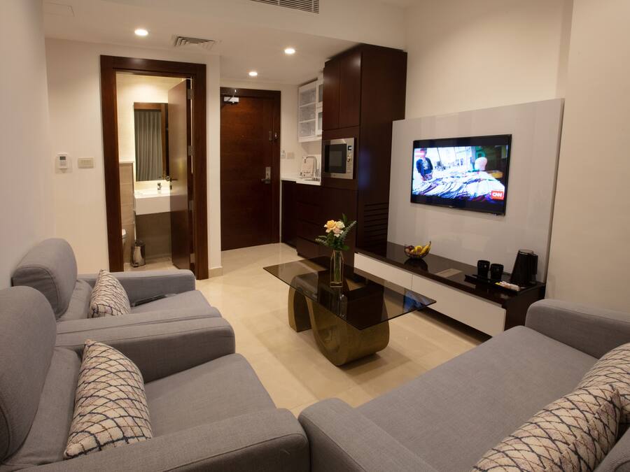 A modern living room with grey sofas, a glass coffee table, a flat-screen TV, and a microwave above a dark cabinet.