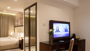 A hotel room with a bed, a desk with a computer, a TV, and a mirror.