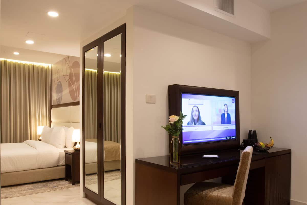 A hotel room with a bed, a desk with a computer, a TV, and a mirror.