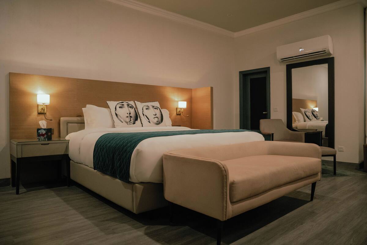 Habitación de hotel con una cama grande, lámparas de noche, una silla, un espejo y un equipo de aire acondicionado.