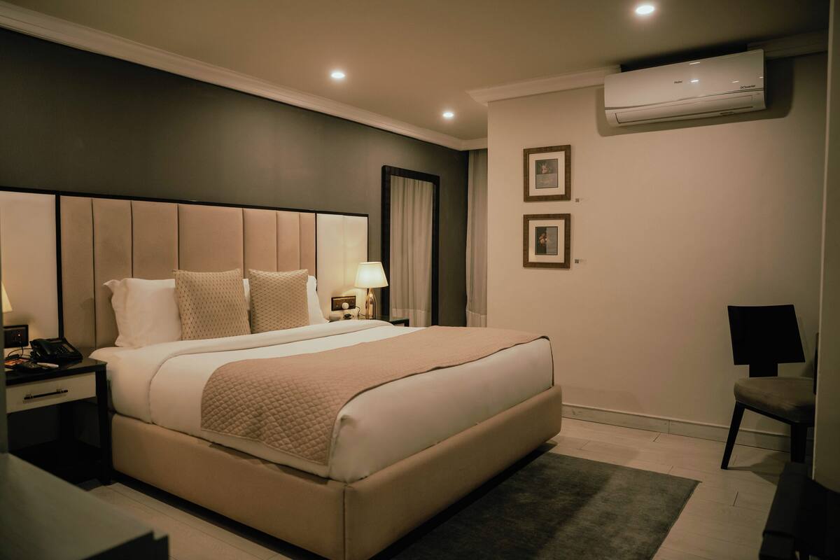 Una habitación de hotel moderna con una cama grande, mesitas de noche, un escritorio y un equipo de aire acondicionado.