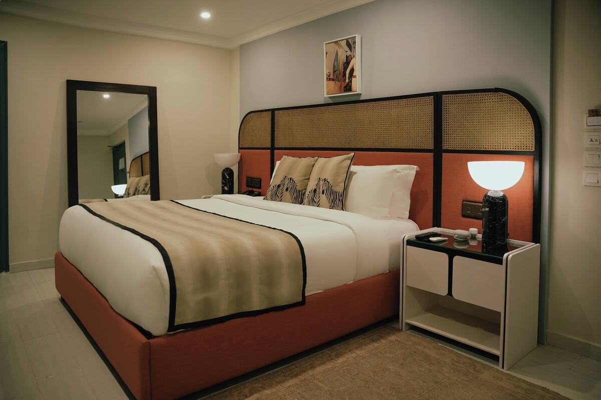 Habitación de hotel moderna con una cama grande, mesitas de noche, un espejo y una obra de arte colgada en la pared.