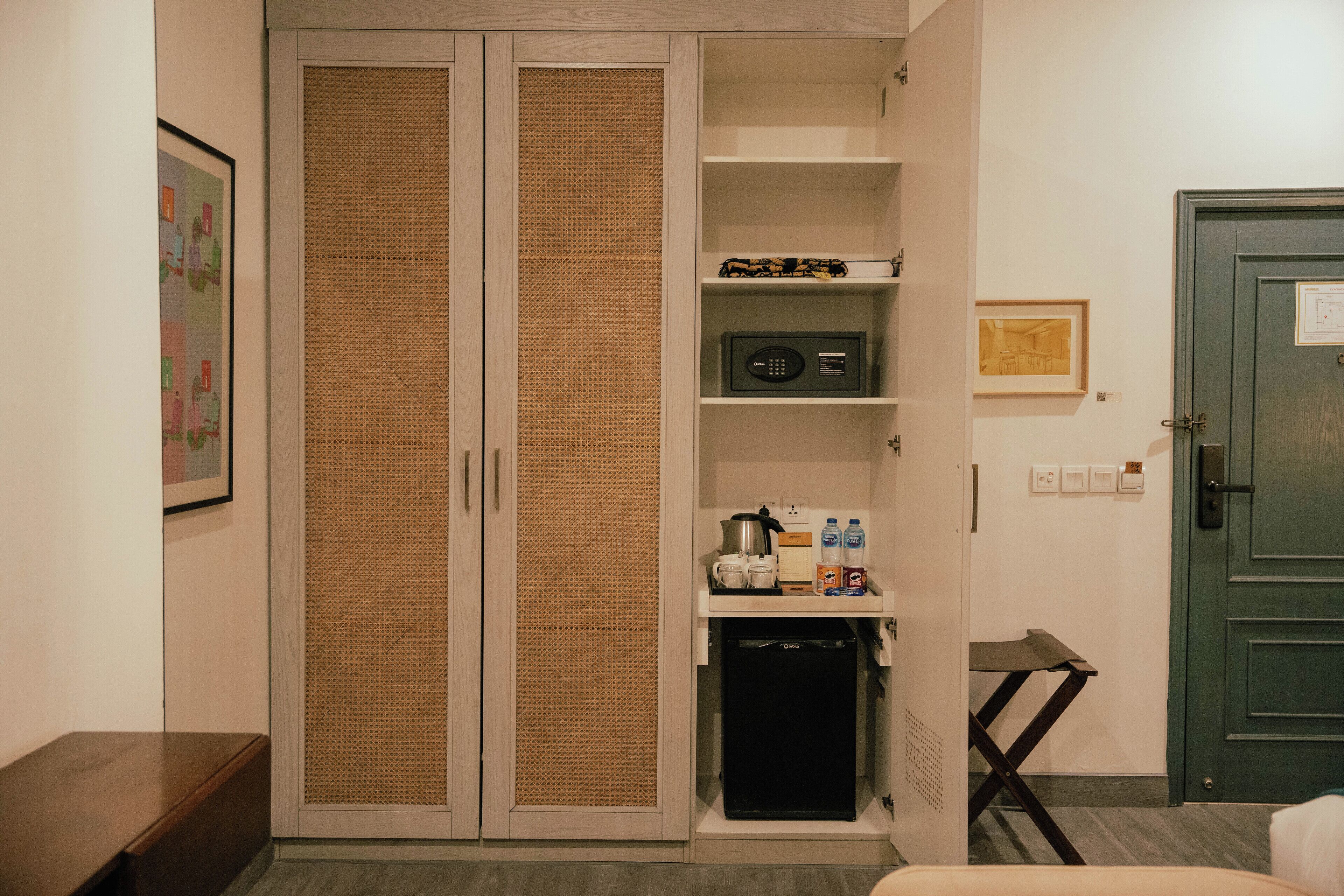 A room with a wardrobe, a small kitchenette, and a door.