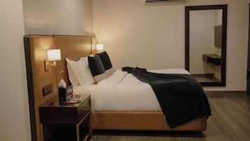A hotel room with a bed, bedside table, lamp, air conditioning unit, and a mirror.