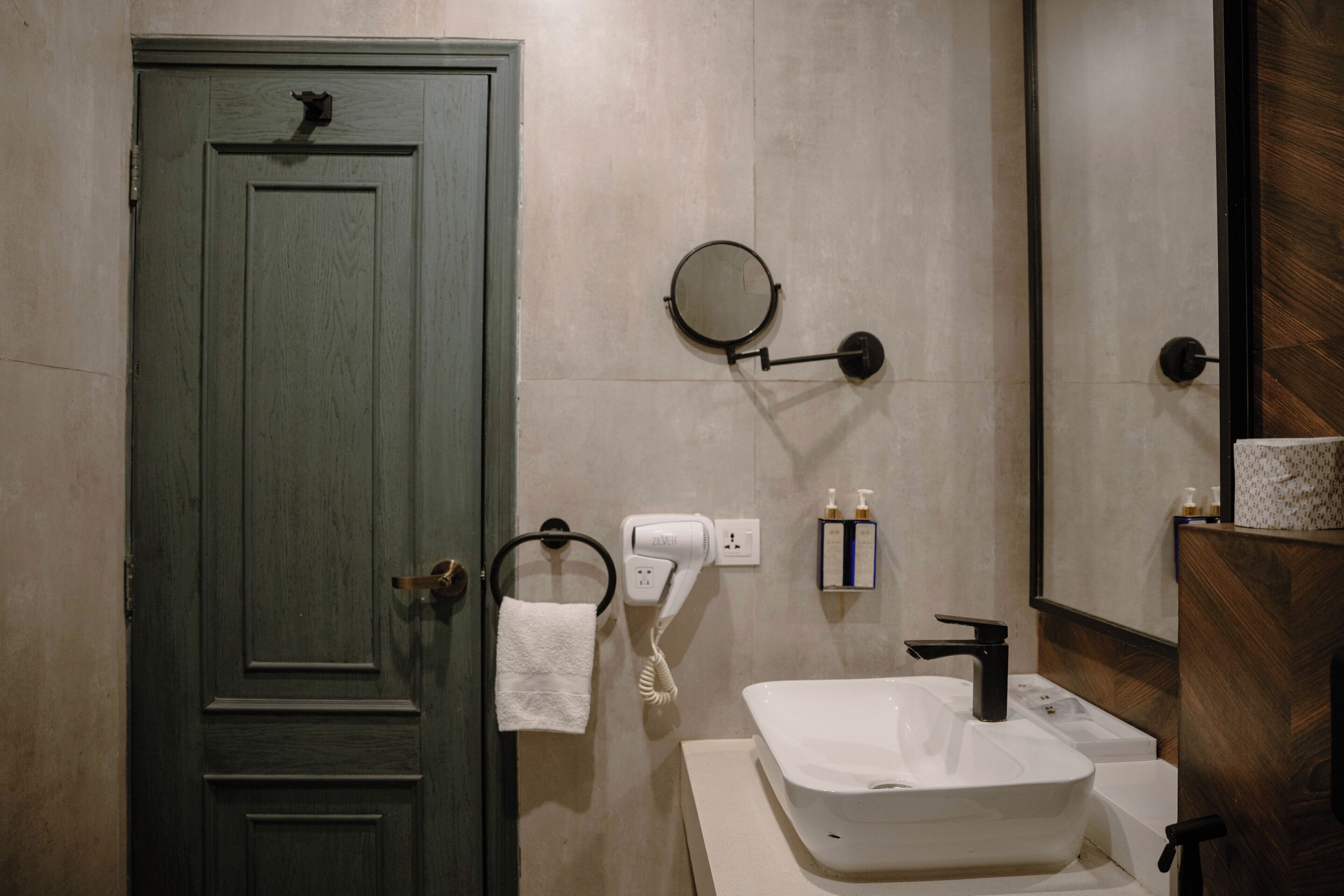 A bathroom with a green door, a round mirror, a white sink, a towel rack, and a hairdryer.