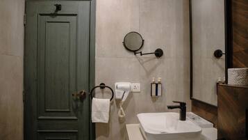 A bathroom with a green door, a round mirror, a white sink, a towel rack, and a hairdryer.