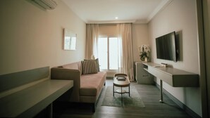 A modern living room with a sofa, a small table, a flat-screen TV, and a window with curtains. -  Ambiance Boutique Art Hotel Karachi (Karachi)