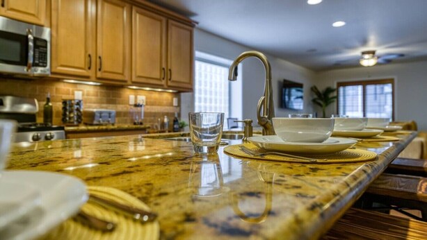 A kitchen with wooden cabinets, a granite countertop, a stainless steel microwave, and a large island with a sink and dining setup.