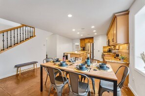 Une cuisine moderne avec des meubles en bois, une table à manger pour quatre personnes et un escalier situé sur le côté gauche.
