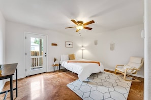 Une chambre à coucher avec un lit, une chaise, un ventilateur de plafond, une porte et une petite table.