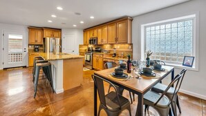 A modern kitchen with wooden cabinets, a central island, stainless steel appliances, and a dining area set for six.