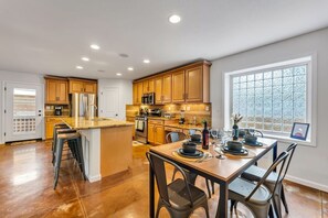 Une cuisine moderne avec des meubles en bois, un îlot central, des appareils électroménagers en acier inoxydable et un coin repas aménagé pour six personnes.