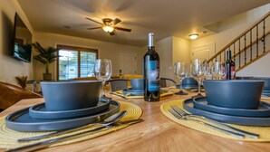A dining table set with plates, bowls, cutlery, and wine glasses, with a bottle of wine in the center.