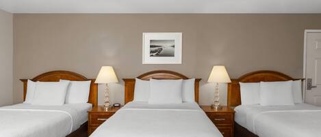 Habitación de hotel con tres camas, cabeceros de madera, mesitas de noche con lámparas y un cuadro en la pared.