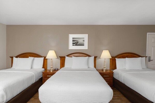 A hotel room with three beds, wooden headboards, bedside tables with lamps, and a framed picture on the wall. - Ramada Bayside Inn & Suites Eureka (Eureka)