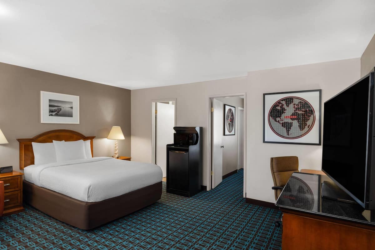 A hotel room with a bed, bedside lamps, a desk with a computer, a TV, and framed pictures on the walls.