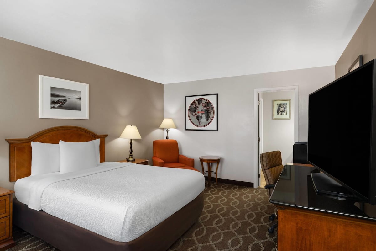 A hotel room with a bed, two chairs, a TV, a lamp, and two framed pictures on the wall.