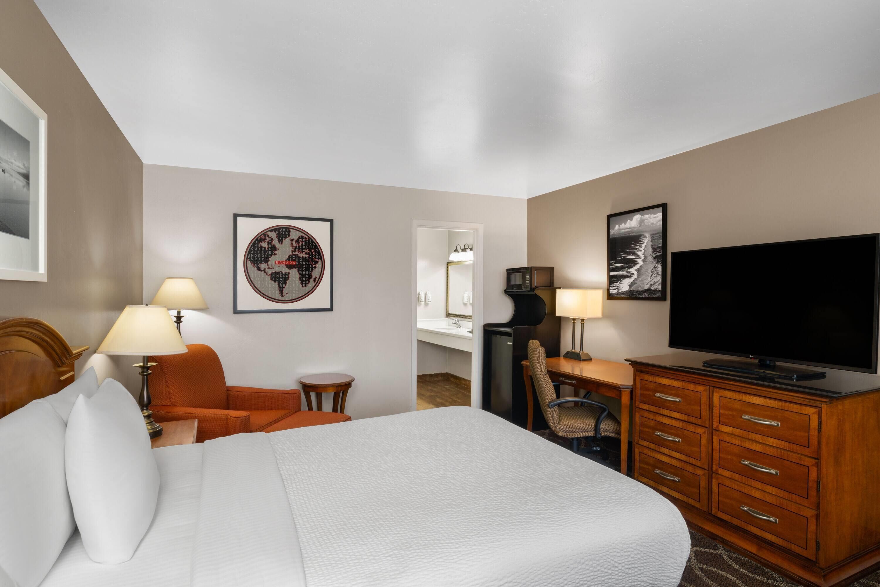 A hotel room with a bed, a desk, a television, a chair, and a lamp.