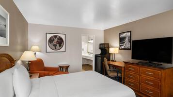 A hotel room with a bed, a desk, a television, a chair, and a lamp.