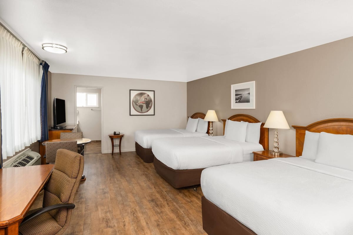 A hotel room with two beds, a desk, a chair, a TV, and a window with curtains.