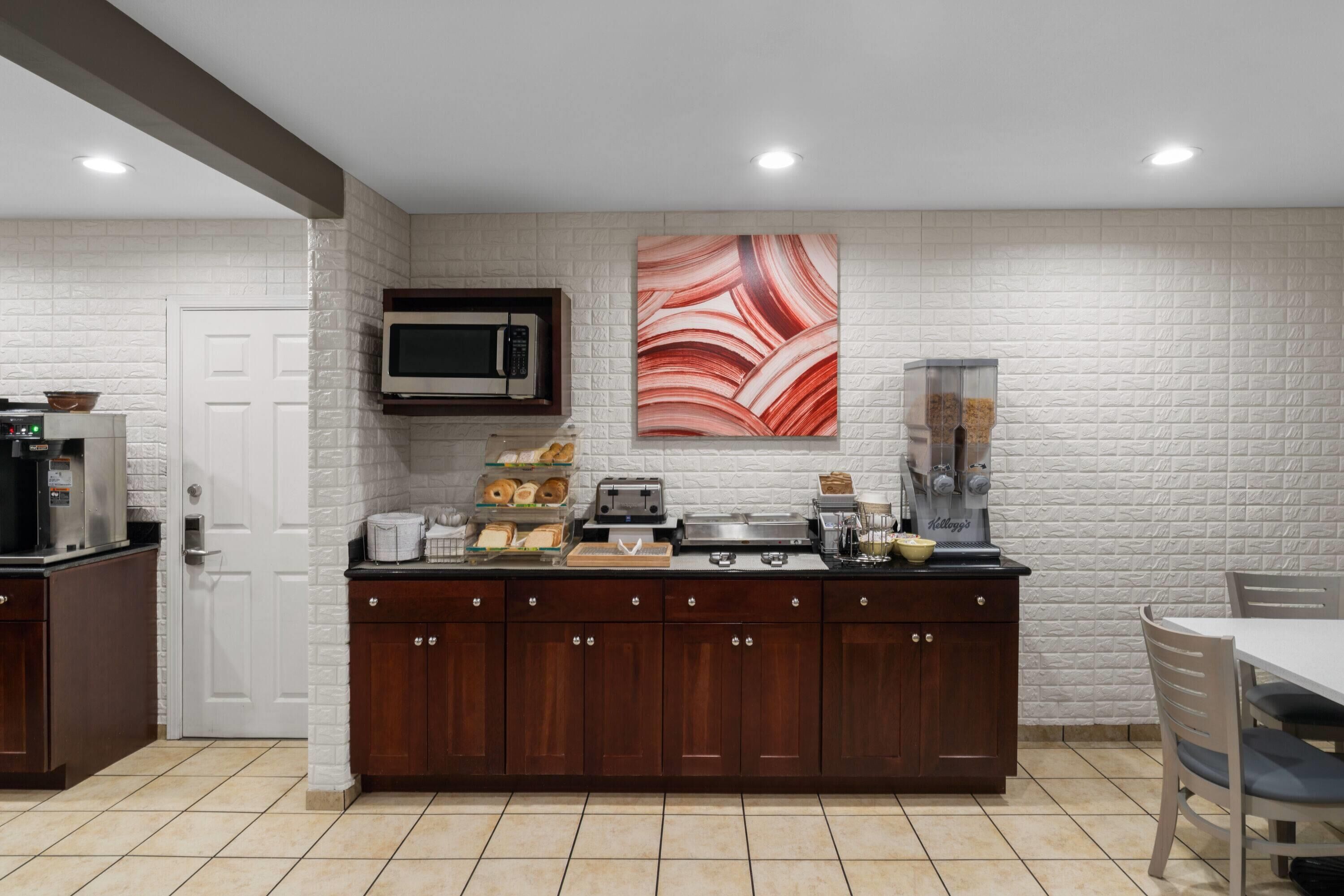 Uma cozinha moderna com parede de tijolos brancos, armários de madeira, micro-ondas, máquina de café e bancada para refeições.