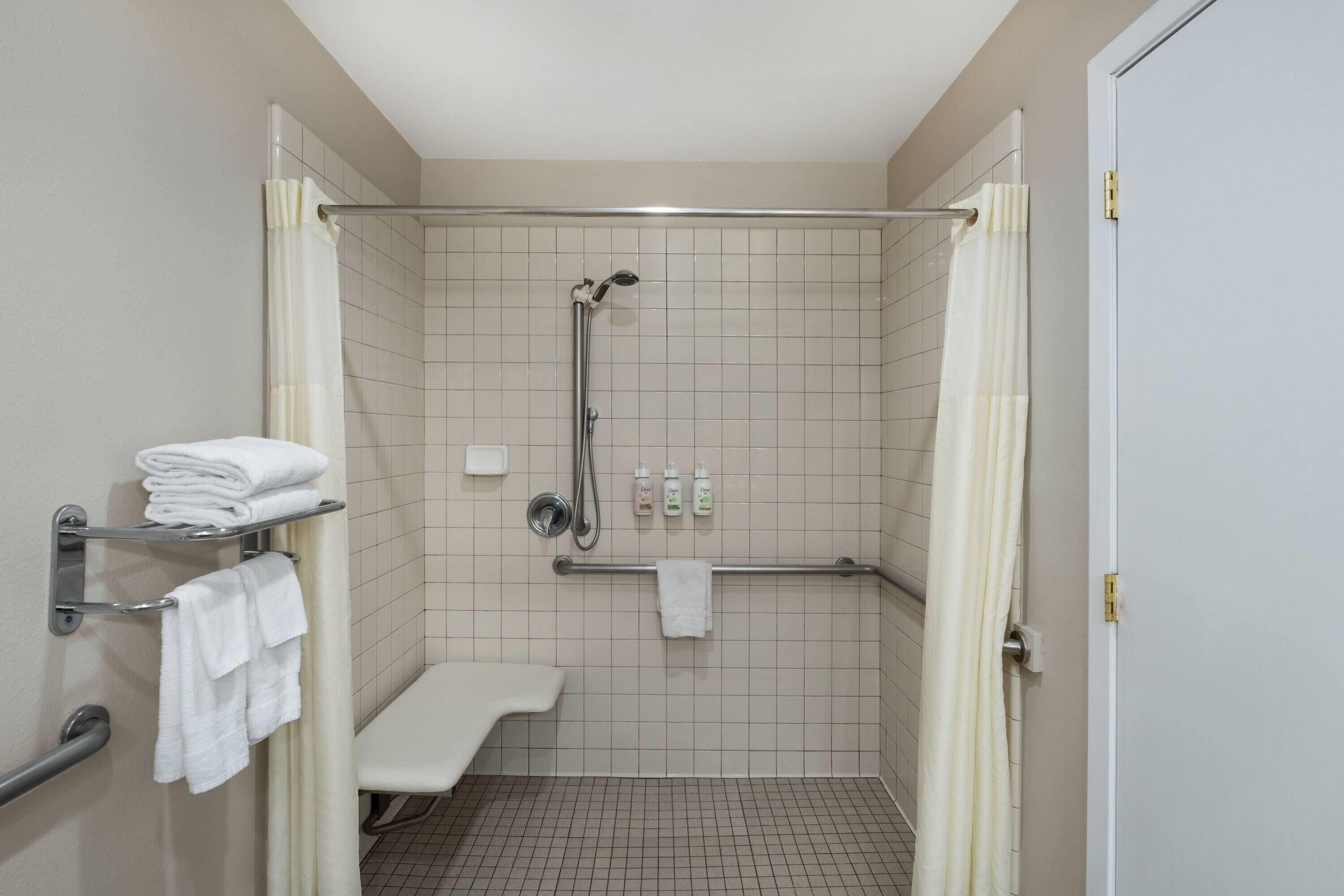 Un baño pequeño y limpio con ducha, un banco y un perchero para toallas.