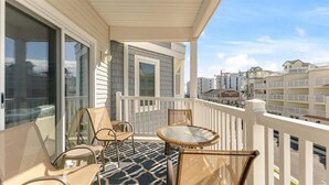 A balcony with a glass table and chairs, a patterned rug, and a view of other buildings. - 3 BR Condo w/ a Pool & Ocean Views Tahitian Condos (Wildwood Crest)