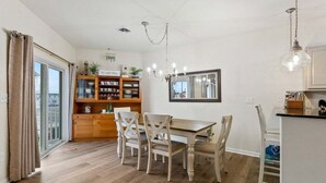A dining area with a wooden table and chairs, a chandelier, and a view through a glass door. - 3 BR Condo w/ a Pool & Ocean Views Tahitian Condos (Wildwood Crest)