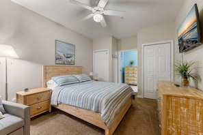 A bedroom with a bed, a nightstand, a dresser, a ceiling fan, and a painting on the wall.