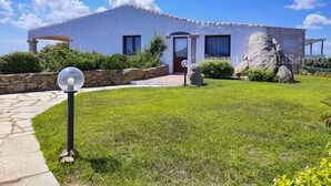 Una casa moderna amb un camí de pedra que condueix a l'entrada, envoltada d'un pràt ic i roques grans.