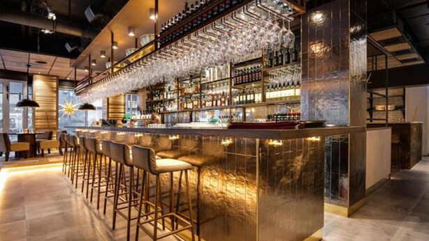 Eine Bar mit einer langen Theke, mehreren Hockern und Regalen voller Flaschen und Gläsern.