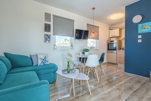 A modern living room with teal sofas, a dining area with white chairs, a kitchen with a stove and oven, and a blue accent wall.