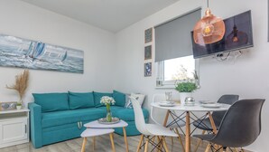 Un salon moderne avec un canapé turquoise, une table basse blanche et un coin repas avec des chaises.