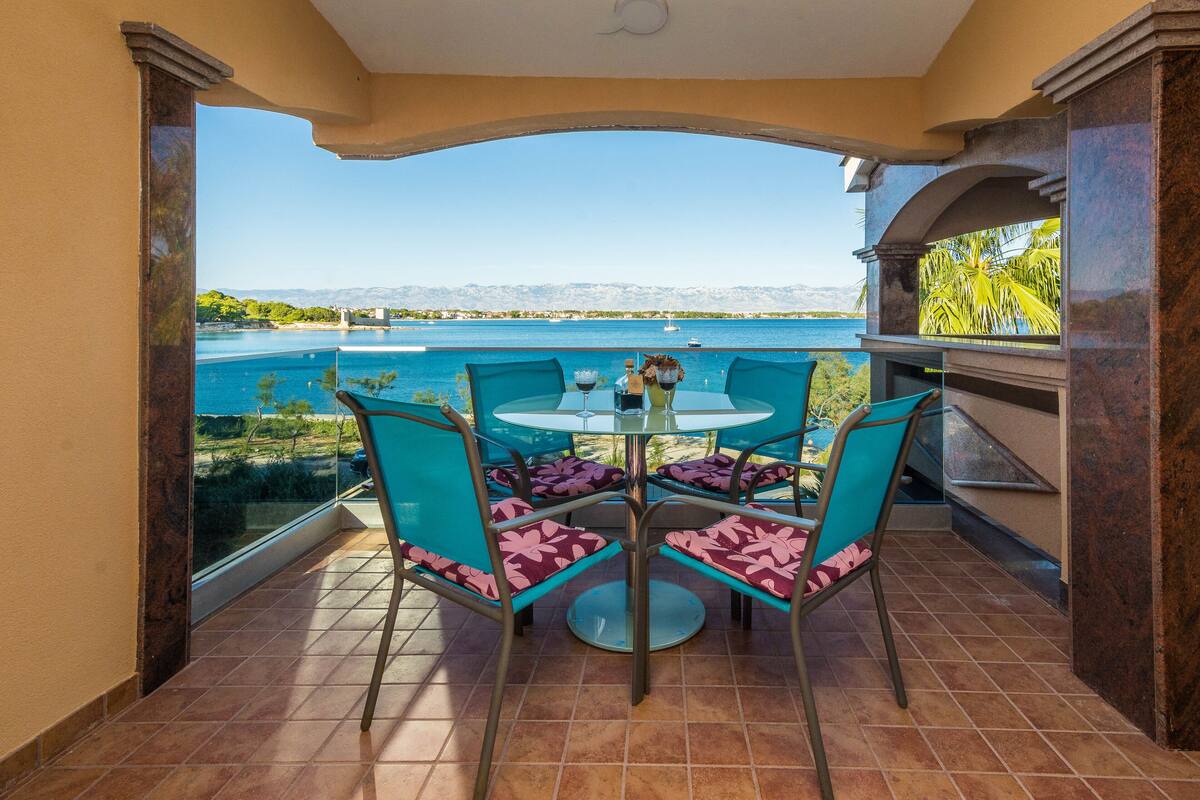Una terraza con mesa y sillas, vista al mar y un paisaje montañoso al fondo.