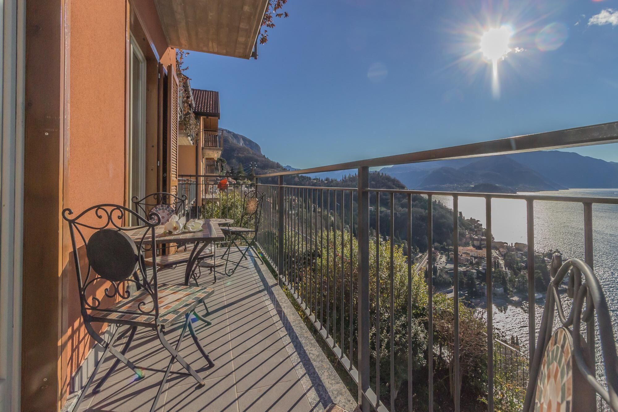 A balcony with a table and chairs, overlooking a lake and mountains.