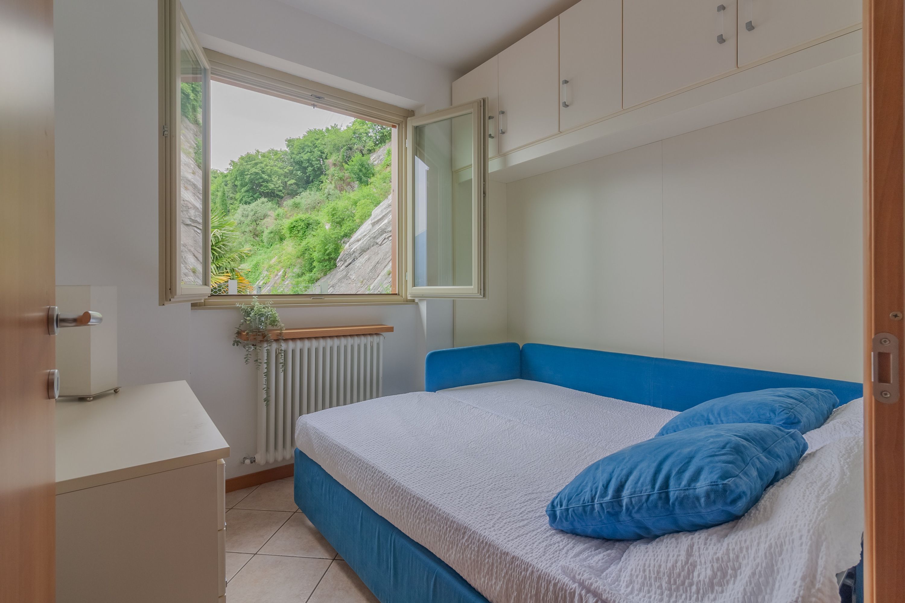 A bedroom with a bed, a window, a radiator, and a small desk.