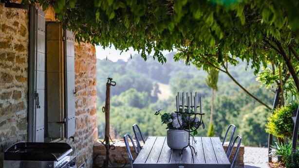 Un espace de restauration en plein air agrémenté d’un mur en pierre rustique, d’une table en bois et d’un chandelier en métal décoré de fleurs.