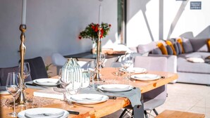 Un coin repas avec une table en bois dressée pour quatre personnes, entouré d’un espace de vie moderne comprenant un canapé et des coussins.