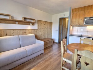 A cozy living area with a sofa, wooden floor, and a dining table with chairs. - Comfortable 2 Rooms, Ski-In/Ski-Out, Close to Shops (La Tania)